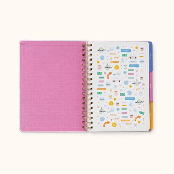 Notebook open showing inside of cover to be a pink with a lighter pink grid, showing the first page including stickers